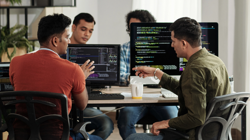 Two computer engineers talk over their code and sit next to each other at a table.